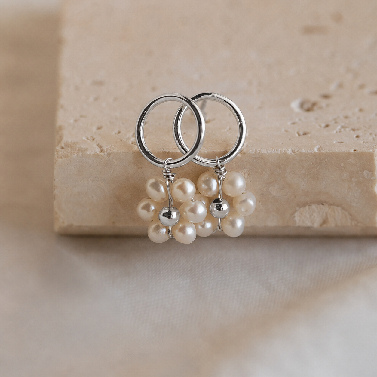 Silver hoop earrings with pearl drops on a beige stone surface